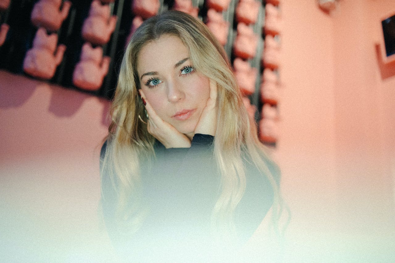 A blonde woman with long hair sitting in front of pink walls